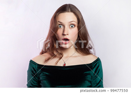 I can't believe this. Portrait of shocked astonished woman wearing green dress, looking at camera with big eyes and open mouth, being very surprised. Indoor studio shot isolated on gray background. I can't believe this. Portrait of shocked astonished woman wearing green dress, looking at camera with big eyes and open mouth, being very surprised. Indoor studio shot isolated on gray background. 99477550