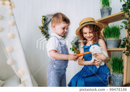 Children feeding white rabbit carrots indoor learning to take care of an animals. Happy childhood  99478186