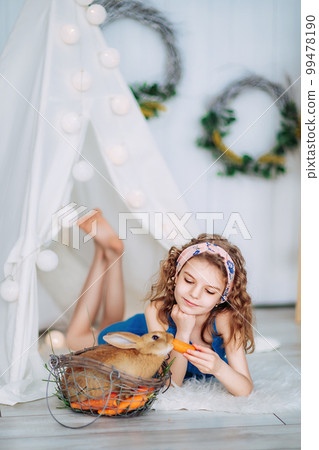 cute little girl laying on the floor and feeding rabbit carrot while learning to take care of animal 99478190