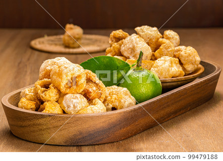 Pile of homemade crispy deep fried pork rinds in wooden tray. 99479188