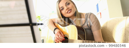 Smiling blond woman playing guitar and looking through notes 99480346