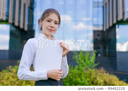 Elegant caucasian business woman in formal wear holds paper documents in her Elegant caucasian business woman in formal wear holds paper documents in her 99482220