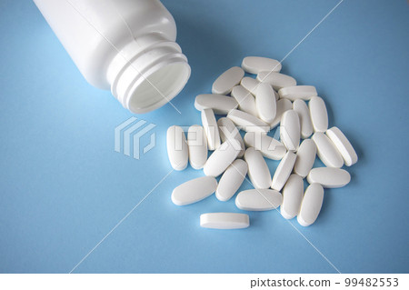 Oval white pills spilled out of the jar on a blue background. 99482553