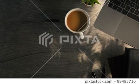 Laptop, cup of coffee and notebook on wooden table with sunlight. Top view with copy space 99483710