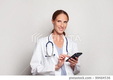 Confident smiling modern mid adult woman doctor medical worker practitioner using smart phone 99484536