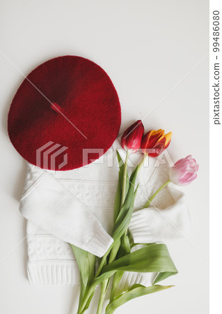 Flat lay white knitted sweater, red hat and bouquet of fresh tulips. Sunday relaxing, vintage mood and lifestyle concept. Cozy spring composition Flat lay white knitted sweater, red hat and bouquet of fresh tulips. Sunday relaxing, vintage mood and lifestyle concept. Cozy spring composition 99486080