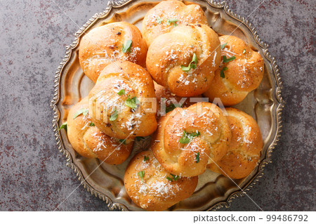 Homemade Buttery Garlic Knot Bread with Parsley and Parmesan cheese and dried greens closeup on the plate. Horizontal top view Homemade Buttery Garlic Knot Bread with Parsley and Parmesan cheese and dried greens closeup on the plate. Horizontal top view 99486792