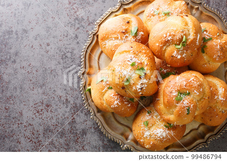 New York Italian garlic knots bread with Parsley and Parmesan cheese and dried greens closeup on the plate. Horizontal top view 99486794
