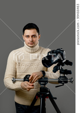 photographer in sweater near digital camera on tripod 99488463