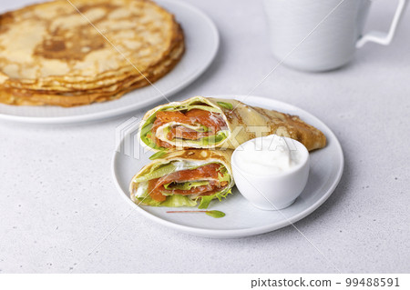 Pancakes with salmon (trout), sour cream and greenstuff. Thin, not sweet blinchiki stuffed with red fish. Traditional Russian and Ukrainian dish. Feast of Maslenitsa. Selective focus, close-up. Pancakes with salmon (trout), sour cream and greenstuff. Thin, not sweet blinchiki stuffed with red fish. Traditional Russian and Ukrainian dish. Feast of Maslenitsa. Selective focus, close-up. 99488591