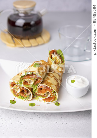 Pancakes with salmon (trout), sour cream, greenstuff and tea. Thin, not sweet blinchiki stuffed with red fish. Traditional Russian and Ukrainian dish. Feast of Maslenitsa. Selective focus, close-up. Pancakes with salmon (trout), sour cream, greenstuff and tea. Thin, not sweet blinchiki stuffed with red fish. Traditional Russian and Ukrainian dish. Feast of Maslenitsa. Selective focus, close-up. 99488594