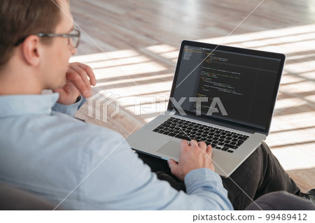 Cropped shot oof coder sitting with laptop on knees Cropped shot oof coder sitting with laptop on knees 99489412