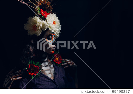 Woman with mexican skull halloween makeup on dark background. Day of the dead aka Dia de los Muertos and halloween concept. Woman with mexican skull halloween makeup on dark background. Day of the dead aka Dia de los Muertos and halloween concept. 99490257