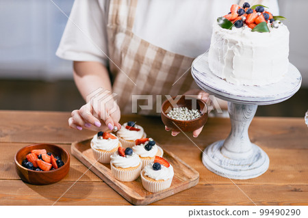 Pastry chef confectioner young caucasian woman decorate sweet balls candy cake on kitchen table. Cakes cupcakes and sweet dessert Pastry chef confectioner young caucasian woman decorate sweet balls candy cake on kitchen table. Cakes cupcakes and sweet dessert 99490290