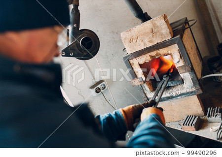 Blacksmith forge oven with hot flame. Smith put in and heating iron piece of steel in fire of red hot forge Blacksmith forge oven with hot flame. Smith put in and heating iron piece of steel in fire of red hot forge 99490296