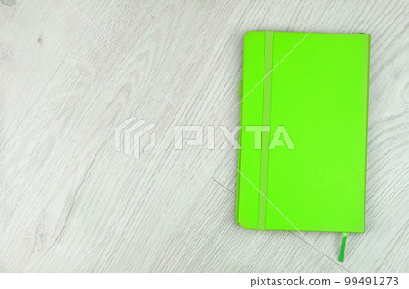 Green notebook on a wooden light background. Closed. Top view. Green notebook on a wooden light background. Closed. Top view. 99491273