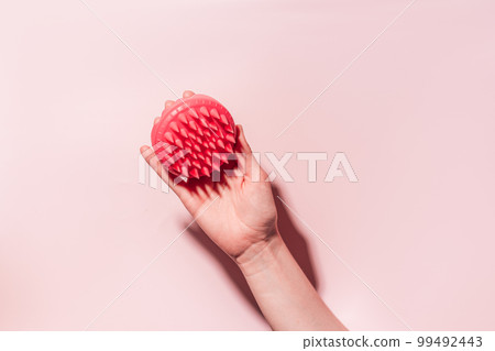 Pink scalp massager in female hand under hard light against pink background 99492443