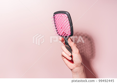 Pink comb in female hand against pink background 99492445