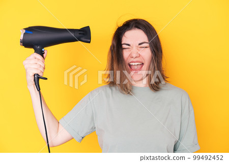 Lady drying her hair with hair dryer against yellow background Lady drying her hair with hair dryer against yellow background 99492452