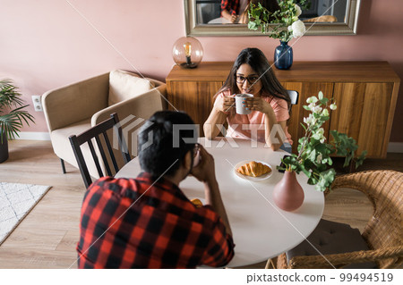 Happy couple eating breakfast and talking at dining table in morning. Indian girl and latin guy. Relationship and diversity concept 99494519
