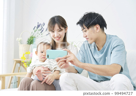 Parents looking at baby and smartphone at home 99494727