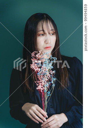A woman in a black dress with dried flowers and a green background 99494859