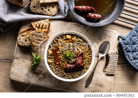 A plate full of lentil legume soup with baked sausage and fresh bread. 99495361