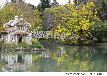 A bird house in the middle of a pond. This beautiful wooden fairy-tale house for swans. 10.10.2022 Russia, Adler, Southern Culture Park Autumn landscape 99496062