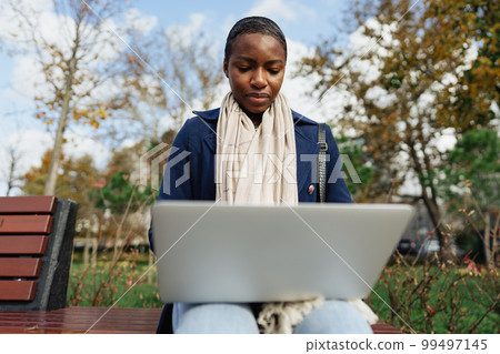 Young african businesswoman using laptop while sitting on the bench in the city Young african businesswoman using laptop while sitting on the bench in the city 99497145
