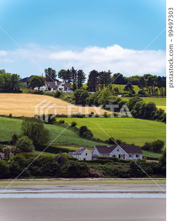 Several buildings and trees on a hill. Irish landscape. Picturesque countryside. Farm fields under a blue sky, house on green grass field. 99497303