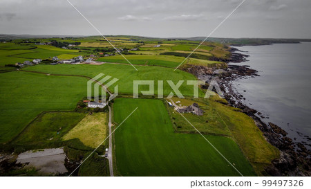 Green fields on the hills, top view. The countryside of Ireland on a cloudy day. The coast of Clonakilty Bay at low tide. Green grass field under cloudy sky 99497326