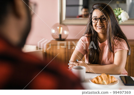 Young diverse loving couple eating croissant and talks together at home in breakfast time. Communication and relationship concept 99497369