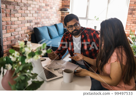 Young millennial indian husband and wife doing domestic paperwork, accounting job and reviewing paper bills, receipts at laptop computer, using online calculator and paying mortgage rent fees on Young millennial indian husband and wife doing domestic paperwork, accounting job and reviewing paper bills, receipts at laptop computer, using online calculator and paying mortgage rent fees on 99497533
