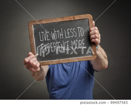 live less to experience more, minimalism and lifestyle concept, white chalk handwriting on a blackboard held by a person live less to experience more, minimalism and lifestyle concept, white chalk handwriting on a blackboard held by a person 99497565