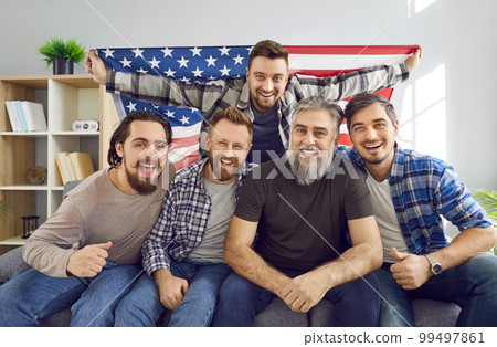Group of men with American flag sitting on couch and watching soccer match on TV 99497861