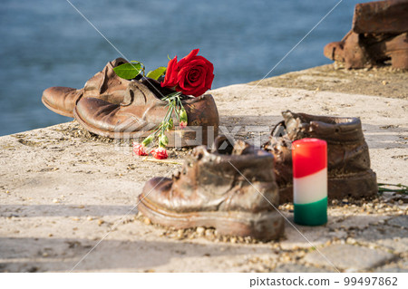 Shoes on the Danube Bank, Budapest, Hungary. Memorial to the Hungarian Jews, the victims of the Holocaust executed along this riverbank during WWII. Red rose and candle. Close-up. 99497862