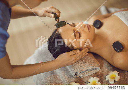 Attractive young woman enjoying facial and hot stone massage 99497863