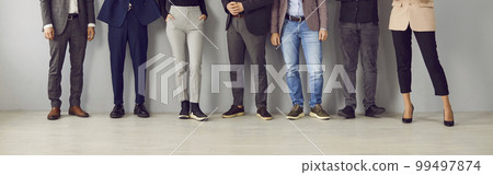 Legs of unrecognizable business people standing in a row on grey office wall bacground. 99497874
