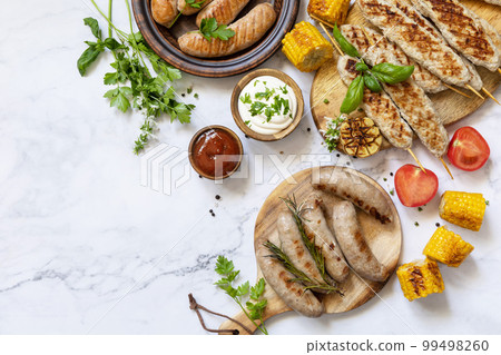 Grill food menu. Various bbq grilled sausages with fresh herbs and spices on marble tabletop. Summer party food. View from above. Copy space. 99498260