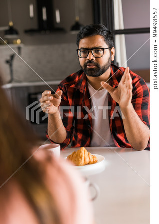 Young diverse loving couple eating croissant and talks together at home in breakfast time. Communication and relationship concept 99498552