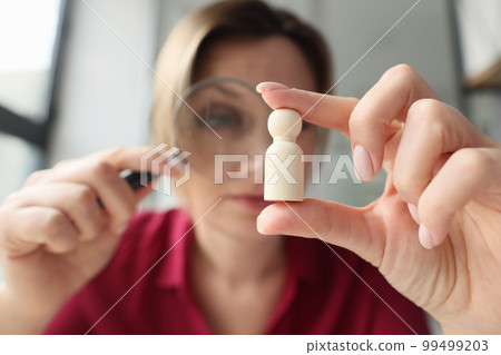Woman looks at a wooden figurine through magnifying glass Woman looks at a wooden figurine through magnifying glass 99499203