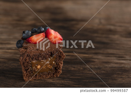 Half of chocolate cupcake with chocolate filling in cut and berries on wooden surface. Fresh chocolate muffin berries. 99499387