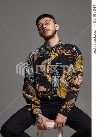 Close-up portrait of a funny guy posing sitting on a bar chair in studio isolated on gray background. 99499844