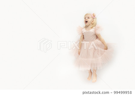 Screaming happy girl in festive dress is jumping. Blonde Little princess isolated on white background. Space for text 99499958