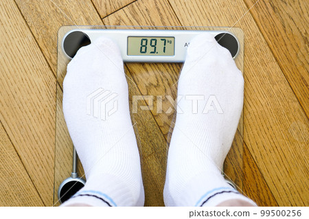 A man in white socks stands on a transparent electronic floor scale, the weight reading is 89 kg 99500256