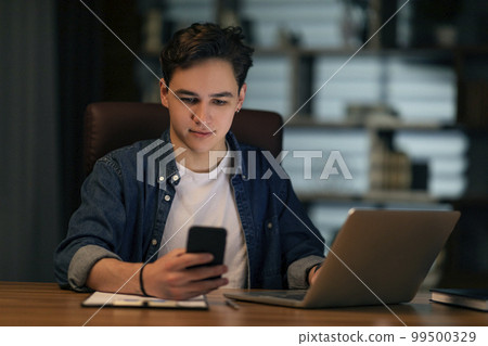 Young guy manager working at office, using laptop and smartphone 99500329