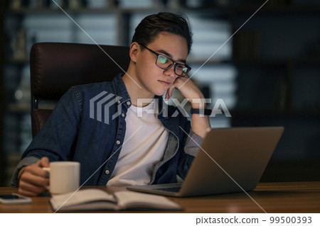 Tired young managaer looking at laptop screen, drinking coffee 99500393