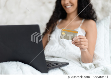 Happy millennial caucasian brunette lady with long hair sitting on soft bed, typing on computer 99500481