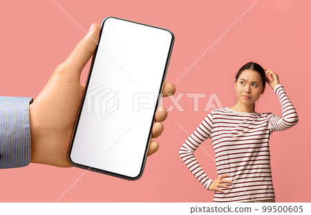 Doubtful Asian Woman Looking Aside At Blank Smartphone In Huge Male Hand 99500605