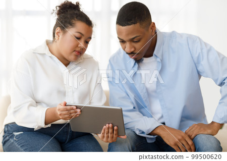 Young hispanic woman psychologist having conversation with patient, showing pad 99500620